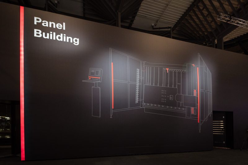 Raumhohe dunkle Wand mit weißer Strichzeichnung einer Maschine und roter Lichtkante